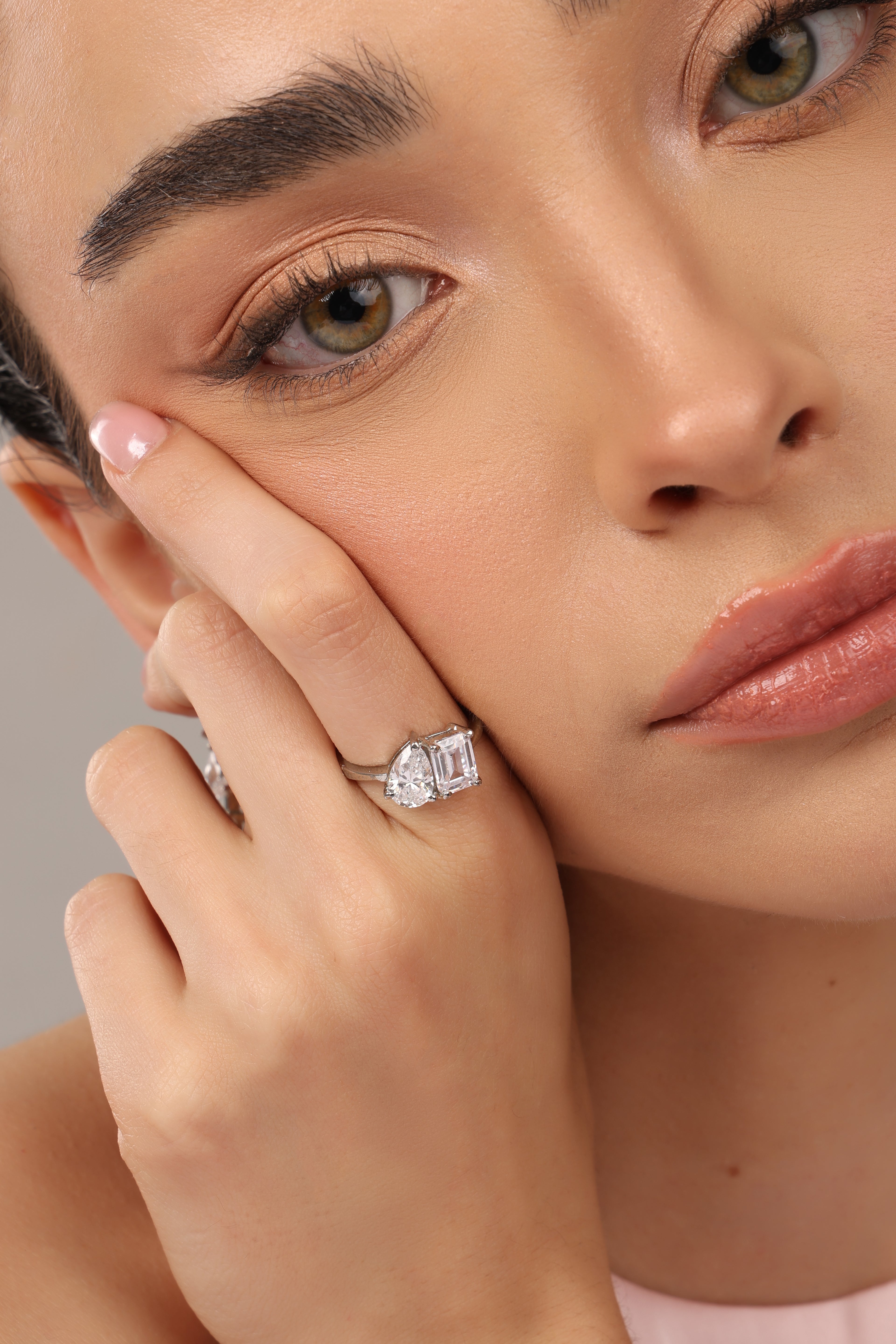 A close-up lifestyle shot of a model wearing a silver ring with three rectangular baguette-cut clear gemstones on her finger, set against a soft neutral background.